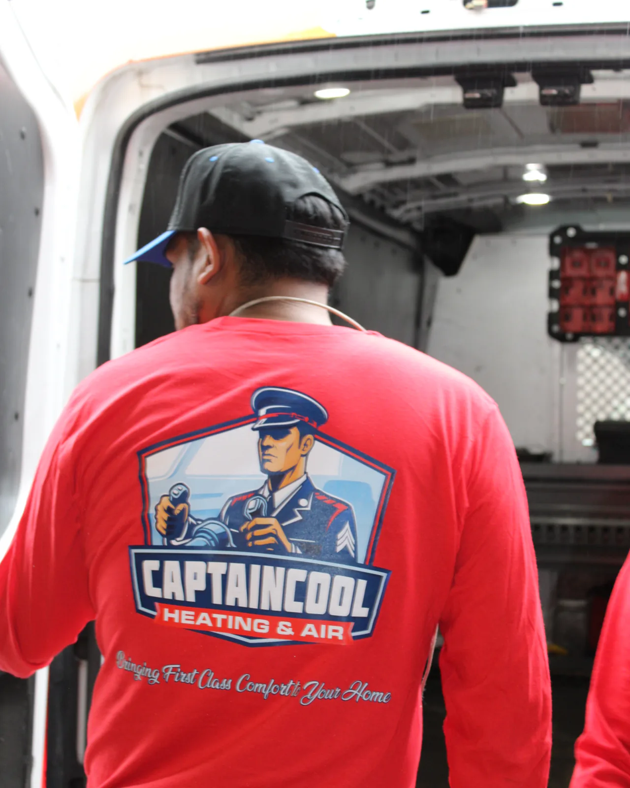 Captain Cool Heating & Air technician with the company logo on the back of his shirt at the open rear doors of a service van